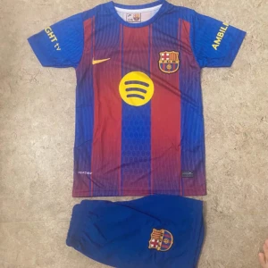FC Barcelona Lamine Yamal fotbollströja - Säljer en FC Barcelona matchtröja med Lamine Yamal och nummer 10 på ryggen. Tröjan är kortärmad med klassiska blå och röda vertikala ränder, gula detaljer och klubbmärke på bröstet. Materialet är lätt polyester, perfekt för träning eller match. Shorts medföljer, också med klubbmärke.