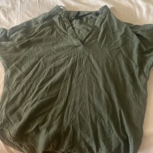 Grön v-ringad t-shirt från Vero Moda - Snygg skogsgrön t-shirt från Vero Moda i storlek M. Modellen är loose fit med korta ärmar och djup v-ringning. Perfekt för dig som gillar en avslappnad och enkel stil. 