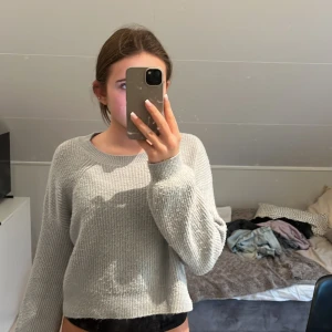 Ljusgrå stickad tröja från KappAhl - Supermysig ljusgrå stickad tröja från KappAhl med rund halsringning och ribbade muddar. Tröjan har en lite croppad passform och långa ärmar, perfekt för lager på lager under kyliga dagar.