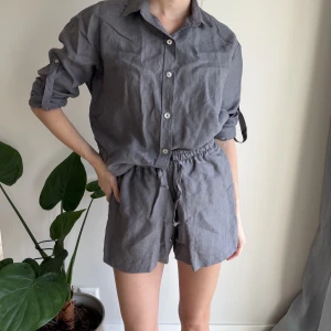 Grå linnen set - Shirt & shorts från Trvlgrl XS - Snygga grå shorts från Trvlgrl (Bali Brand) i luftig linnekvalitet. Modellen är loose fit med hög midja och elastisk midja med snörning för extra komfort. Perfekta för varma dagar och ger en chill vibe till din outfit. Shorts är mer XXS