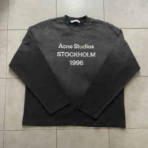 Svart långärmad tröja Acne Studios - Svart långärmad tröja från Acne Studios med tryck 'STOCKHOLM 1996' på bröstet. Tröjan har en klassisk rund hals och är tillverkad i mjuk bomull. Passformen är normal och stilen är enkel men snygg, perfekt för dig som gillar minimalistisk design.