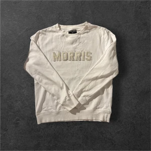 Vit sweatshirt från Morris - Vit sweatshirt från Morris med broderad logga framtill i offwhite. Klassisk rund halsringning, ribbade muddar och lång ärm. Skön och stilren tröja i bomull som passar perfekt till jeans eller chinos.