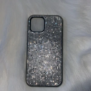 iPhone 12/12 Pro Glittrande Skal - Snyggt skal till iPhone 12/12 Pro med glittrande diamanter  som ger din mobil ett exklusivt utseende. Skalets skick är mycket bra, utan synligt slitage eller repor. Perfekt för dig som vill skydda din telefon. Skalet går tappat några diamanter men inget som stör!