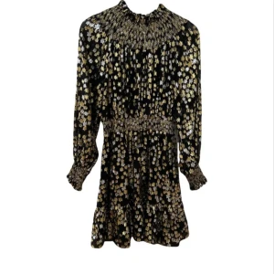 Svart och guld glittrig kortklänning - Supersnygg svart kortklänning med glittrigt guldmönster och smockdetaljer vid hals, midja och ärmslut. Klänningen har långa ärmar och ett flowy fall med volang nertill. Perfekt för dig som vill sticka ut med en glamorös look.