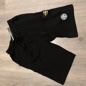 Svarta shorts från Stone Island - Svarta shorts från Stone Island med klassisk logopatch på benet och broderad emblem. De har en loose passform, elastisk midja med snörning och är gjorda i mjuk bomull. Perfekta för chill dagar och streetwear-stil.