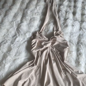 Beige omlottklänning med knut - Supersnygg beige klänning med omlottdesign och knutdetalj framtill. Klänningen har breda axelband och en flowy kjol som ger en feminin siluett. Perfekt för dig som gillar stilrena och trendiga plagg i ljusa toner.