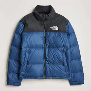 Blå pufferjacka från The North Face - Säljer en blå pufferjacka från The North Face med svart axelparti och logga på bröstet. Jackan har hög krage, två sidofickor med dragkedja och quiltad design. Perfekt för kalla dagar och har en snygg, sportig look.    Pm för bilder