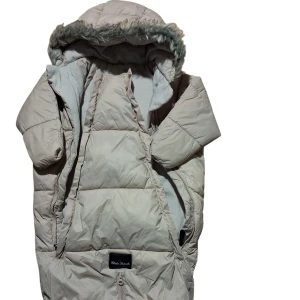 Beige pufferjacka med fuskpäls - Säljer en beige pufferjacka från Eddie Penella med huva och fuskpäls. Jackan har långa ärmar, quiltad design och dragkedja framtill. Perfekt för kalla dagar med sin varma och fluffiga look. Snyggt märke på framsidan och stilren färg.