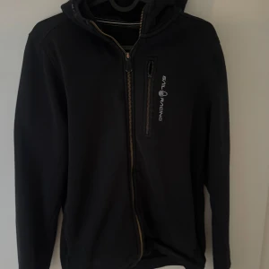 Hoodie Sail racing  - Svart zip hoodie från Sail racing. Fickan vid bröstet har tappat den dragkedja saken, men den ligger i fickan. 