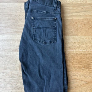 Svarta jeans från Tiger of Sweden - Snygga svarta jeans från Tiger of Sweden med klassisk femficksdesign. Jeansen har silverfärgade nitar och diskret logga vid myntfickan. Perfekt passform och stilren look som funkar till det mesta. Liknar Replay ambass i passformen. 