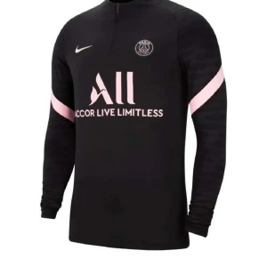 Svart PSG Långärmad Tröja - Svart långärmad fotbollströja från Nike för PSG med rosa detaljer och klubbmärke på bröstet. Tröjan har halv dragkedja, diskret mönster på ärmarna och tryckt sponsorlogga framtill. Perfekt för dig som vill sticka ut på planen.