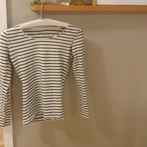 Randig långärmad tröja från Lindex - Säljer en vit och svart randig långärmad tröja från Lindex. Tröjan har en rund halsringning och är gjord i mjuk bomull, perfekt för dig som gillar enkel och stilren design. Passar dig som vill ha en klassisk look med smal passform.