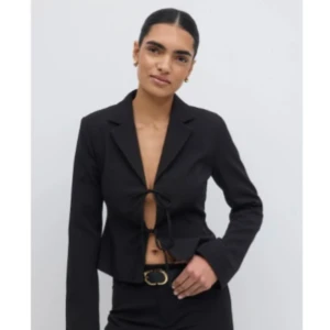 Svart croppad kavaj med knyt från Gina Tricot  - Snygg svart croppad kavaj med knyt framtill och klassisk krage i nyskick. Kavajen har lång ärm och en stilren, figurnära passform som ger en modern look. Ny pris 599kr från Gina Tricot. 