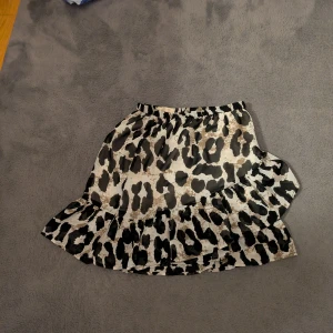 Kort volangkjol med leopardmönster - Snygg kort kjol med leopardmönster i svart, beige och vitt. Kjolen har volang nertill och resår i midjan för en bekväm passform. 