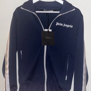 Mörkblå Palm Angels, ÄKTA, storlek S - Säljer en snygg marinblå trackjacka från Palm Angels med vita ränder längs ärmarna och vit dragkedja. Jackan har bara används vid fåtal tillfällen, alltså är den i nyskick
