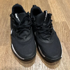 Svarta Nike Air Max sneakers - Säljer ett par svarta Nike Air Max sneakers med vit swoosh och detaljer. Ovandelen är i mesh och syntet, med snörning och platt sula. Skorna har en sportig vibe och passar perfekt för dig som gillar streetstyle och komfort.