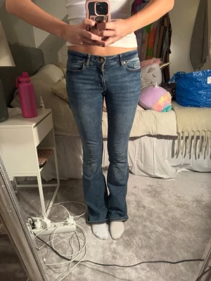 Blå bootcut jeans med låg midja - Snygga blå bootcut jeans med låg midja och klassisk femficksdesign. Jeansen har en lätt tvättad look och sitter tajt över låren för att sedan bli vidare nedtill. Perfekta till sneakers eller boots och ger en avslappnad men trendig vibe.