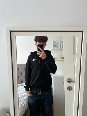Svart kofta från The North Face - Säljer en svart hoodie från The North Face med dragkedja och huva. Klassisk logga på bröstet och två stora fickor framtill. Perfekt för en chill och stilren look. Mjuk bomullskänsla och ribbade muddar vid ärmslut och nederkant. Storlek S.