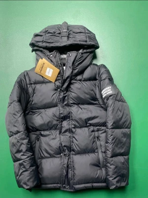 Burberry jacka  - Stilren svart dunjacka från Burberry med huva och quiltad design. Jackan har dragkedja och knappar framtill, två fickor med dragkedja och Burberry-logga på armen. Perfekt för kalla dagar och ger en modern look. Priset kan diskuteras vid seriös affär 🤝