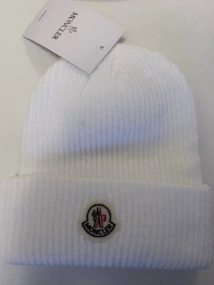 Vit ribbstickad mössa från Moncler - Snygg vit ribbstickad mössa från Moncler med uppvikt kant och klassisk Moncler-logga framtill. Tillverkad i mjukt material som håller dig varm och stilren under kalla dagar. Perfekt accessoar för dig som vill ha en clean och exklusiv look.