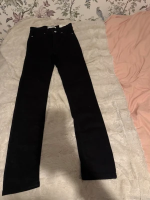 Svarta raka jeans från Gina Tricot - Svarta jeans med rak passform från Gina Tricot. Klassisk femficksmodell med silverfärgade knappar och nitar. Jeansen har hög midja och är tillverkade i bomull med en liten andel stretch för extra komfort.