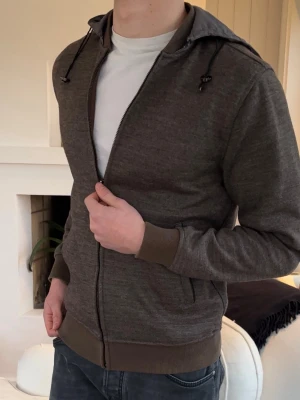 Massimo Dutti cardigan  - Mörkbrun hoodie med dragkedja och ribbade muddar. Huva med dragsko och grått innerfoder. Två fickor framtill. Perfekt för en avslappnad stil.