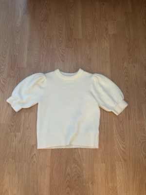 Vit stickad tröja med puffärm - Säljer en söt vit stickad tröja med puffärmar och ribbade muddar. Tröjan har rund halsringning och kortare passform, perfekt för att skapa en trendig look. Materialet känns mjukt och bekvämt, och de voluminösa ärmarna ger en extra touch till outfiten.