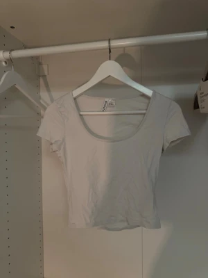 Vit crop top från Divided - En basic vit crop top från Divided med rund halsringning och korta ärmar. Tillverkad i mjuk bomull, perfekt att matcha med jeans eller kjol för en enkel och clean look. Finns en ytterst liten fläck på baksidan av t-shirten, se sista bilden. Den syns inte på långt håll🤍