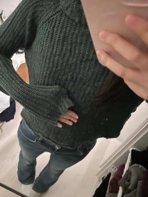 Mörkgrön stickad polotröja - Mysig mörkgrön stickad tröja med polokrage och lång ärm. Tröjan har en ribbad struktur och sitter lite loose för en avslappnad look. Perfekt för kyligare dagar och enkel att styla med jeans eller kjol. På båda sidorna så finns det hål för snygga stil och ger coolare vibe.