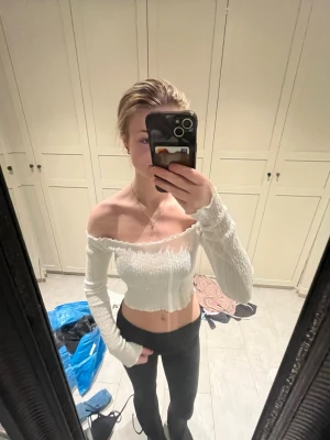 Vit offshoulder croppad topp - Trendig vit croppad topp med offshoulder och långa ärmar. Toppens material är stretchigt och har en smockad struktur som ger en snygg passform. 