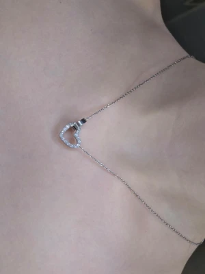 Halsband med hjärta från Edblad - Snyggt halsband i silverfärgat stål från Edblad med ett hjärta dekorerat med små gnistrande stenar och en ring som hänger i kedjan. Perfekt accessoar för att lyfta din outfit med en elegant touch.