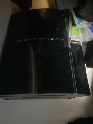 PlayStation 3 svart konsol med 2 kontroller - Säljer en klassisk svart PlayStation 3 konsol från Sony. Konsolen har en blank finish och den ikoniska böjda designen med PlayStation 3-loggan på ovansidan. Perfekt för dig som vill spela äldre PS3-spel eller använda som mediacenter. Har en massa spel som du får med det är över 10 stycken