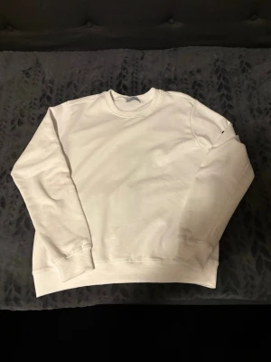 Vit sweatshirt från Stone Island - Klassisk vit sweatshirt från Stone Island med rund halsringning och ribbade muddar vid ärmslut och nederkant. Enkel och stilren design som passar till det mesta. Tillverkad i mjukt material för skön komfort.