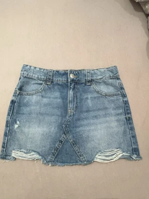 Blå jeanskjol med slitna detaljer - Jag säljer en jeanskjol med slits nedtill med knapp bakfickor. En vanlig knapp och dragkedja vid midjan. Skriv gärna vid frågor💕