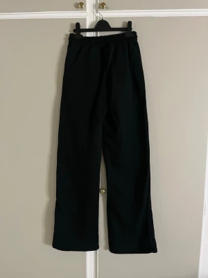 Svarta mjukisbyxor från Ralph Lauren - Svarta mjukisbyxor från Ralph Lauren med rakt ben och elastisk midja. Klassisk röd broderad logga på benet. Tillverkade i mjukt bomullsmaterial som känns skönt mot huden. Perfekta för chill dagar eller när du vill ha en clean och enkel look.