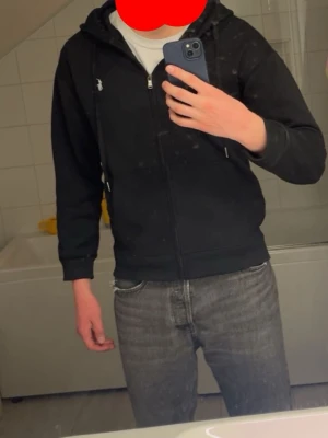 Svart hoodie från Polo Ralph Lauren - Svart hoodie med dragkedja från Polo Ralph Lauren. Klassisk design med vit broderad logga på bröstet, huva med dragsko och känguruficka. Perfekt för en chill och stilren look.