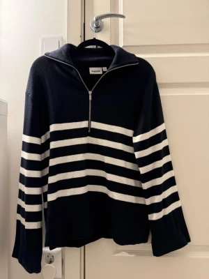 Randig stickad tröja från Kappahl - Mörkblå stickad tröja med vita horisontella ränder från Kappahl. Tröjan har halv dragkedja framtill, krage och långa ärmar. Perfekt för en avslappnad och trendig look.