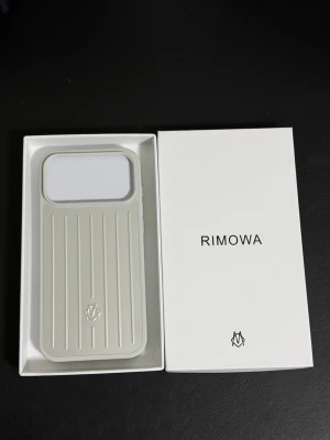 Rimowa Iphone 17 pro max silverfärgat mobilskal  - Snyggt och stilrent mobilskal från Rimowa i en ljus silverfärg med klassisk räfflad design. Skalet är tillverkat i tålig plast och har en stor öppning för kameran. Passar perfekt för dig som vill ha ett exklusivt och modernt skydd till din iPhone.