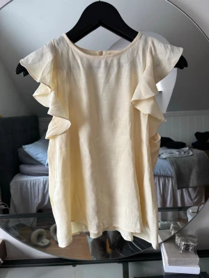 Ljusgul volangtopp från Zara - Supersöt ljusgul topp från Zara med volangdetaljer längs ärmarna. Toppen är ärmlös och har en lös passform som ger en luftig känsla. Perfekt för varma dagar och enkel att styla med dina favoritjeans eller kjol. Aldrig använd med prislapp kvar! Stl xs