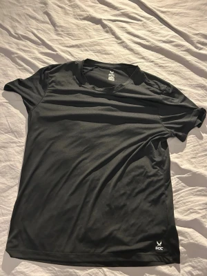Svart sportig t-shirt från SOC - En svart t-shirt från SOC i sportig modell med rund hals och korta ärmar. Tillverkad i ett lätt och snabbtorkande syntetmaterial som passar perfekt för träning. Diskret logga nere vid fållen framtill. 