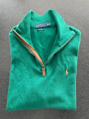 Grön halvzip från Polo Ralph Lauren - Snygg grön tröja från Polo Ralph Lauren med halv dragkedja och klassisk broderad logga på bröstet. Tillverkad i bomull med ribbade detaljer och hög krage. Perfekt för dig som gillar stilrena och tidlösa plagg.