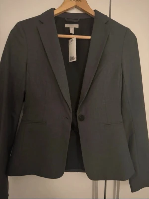 Mörkgrå kavaj från H&M -  mörkgrå kavaj från H&M med klassisk krage och enkel knäppning framtill. 