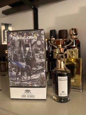 Penhaligon's Lord George parfym - Unik parfymflaska från Penhaligon's Portraits-serie, The Tragedy of Lord George. Flaskan har en elegant guldfärgad hjorthuvud-kork och klassisk etikett. Förpackningen har ett konstnärligt svartvitt motiv med detaljer i färg. Perfekt för dig som gillar lyxiga och kreativa dofter.