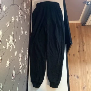 Svarta mjukisbyxor från Berga  - Svarta mjukisbyxor från Berga i storlek S. Byxorna har resår i midjan med snörning och muddar vid bensluten. Tillverkade i en mjuk blandning av bomull och polyester, perfekta för chill dagar. Klassisk och enkel design.