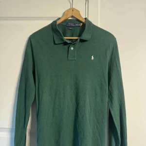 Grön långärmad pikétröja Polo Ralph Lauren - Snygg grön långärmad pikétröja från Polo Ralph Lauren i slim fit-modell. Klassisk krage med två knappar och den ikoniska broderade loggan på bröstet. Perfekt för dig som gillar stilrena och tidlösa plagg.
