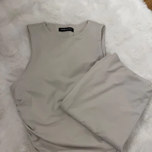 Beige ärmlös topp med en matchade lång kjol från SHEIN BAE - Säljer en stilren beige ärmlös topp från SHEIN BAE i storlek M. Toppen har en rund halsringning och är figurnära med lätt rynkade sidor med en matchade långt kjol. Materialet är mjukt och stretchigt, perfekt för en clean och modern look.