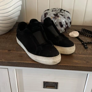 Axel arigato laceless - Snygga svarta sneakers från Axel Arigato med vit platt sula och minimalistisk design. Ovandelen är i mocka och skon har en stilren look utan synlig snörning. Perfekta för dig som gillar en clean och modern stil.