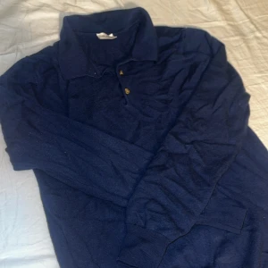 Marinblå pikétröja 100% merino från John Henric - Snygg marinblå långärmad pikétröja 100% merino från John Henric. Klassisk krage och knäppning med två knappar framtill. Tröjan är gjord i mjukt material och har ribbade muddar vid ärmsluten. Perfekt för en stilren och avslappnad look. Passar xs, priset är diskuterbart 