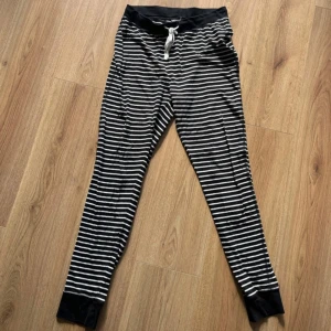 Randiga svarta mjukisbyxor med snörning - Svarta mjukisbyxor med vita horisontella ränder, bred resår och snörning i midjan samt muddar vid bensluten. Byxorna har en bakficka och är gjorda i mjukt bomullsmaterial, perfekta för chill dagar hemma.