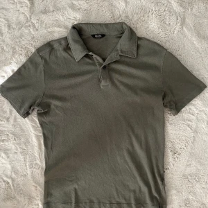 Grön pikétröja från Massimo Dutti - Snygg grön pikétröja från Massimo Dutti med klassisk krage och korta ärmar. Tillverkad i en mjuk mix av linne och bomull som känns skön mot huden. Perfekt för dig som gillar stilrena och enkla plagg med en chill vibe.